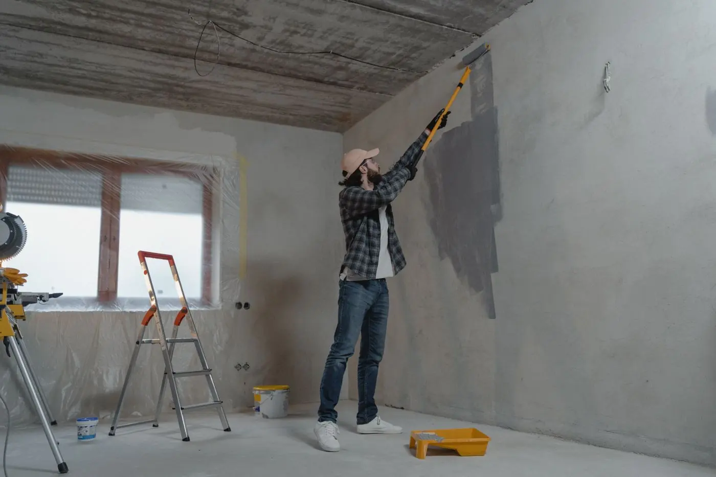 Man verft een grijze muur met een verfroller op een lange steel naast een trap